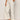 A person wears Sanctuary Clothing's lily cropped pant in setting sun stripe (petite sizing), featuring beige wide-leg, high-waisted, drawstring pants with thin vertical stripes, paired with white sneakers detailed in beige.