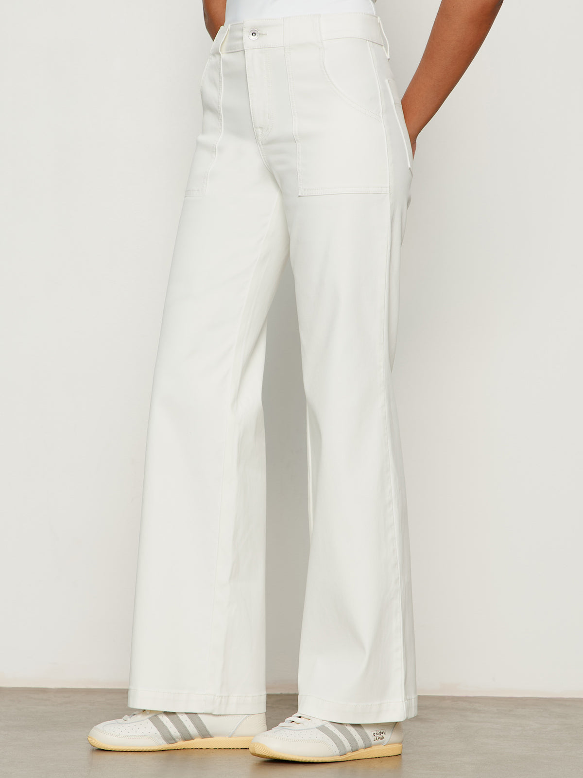 A person wears Sanctuary Clothing's sculpted insider wide leg pant in chalk with visible front pockets and white sneakers with light gray stripes, standing against a plain background.