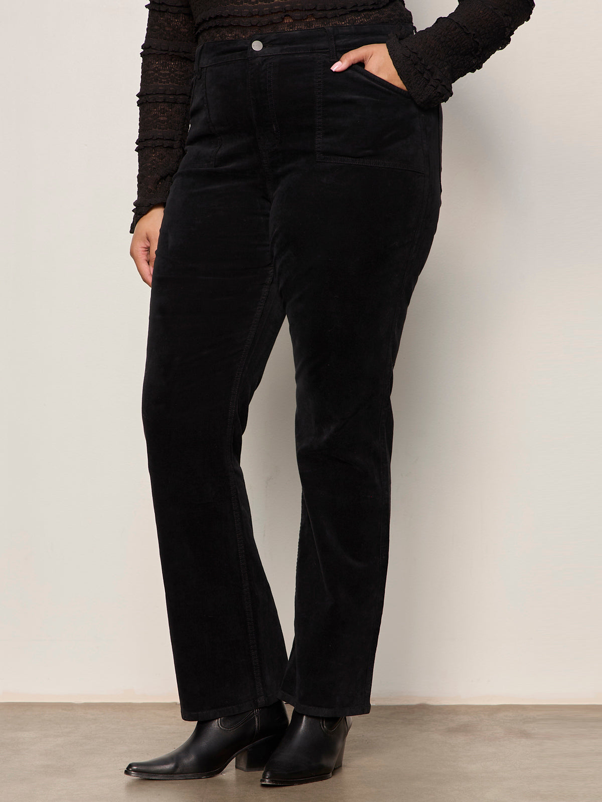 Person wearing black velvet pants and black shoes against a plain background