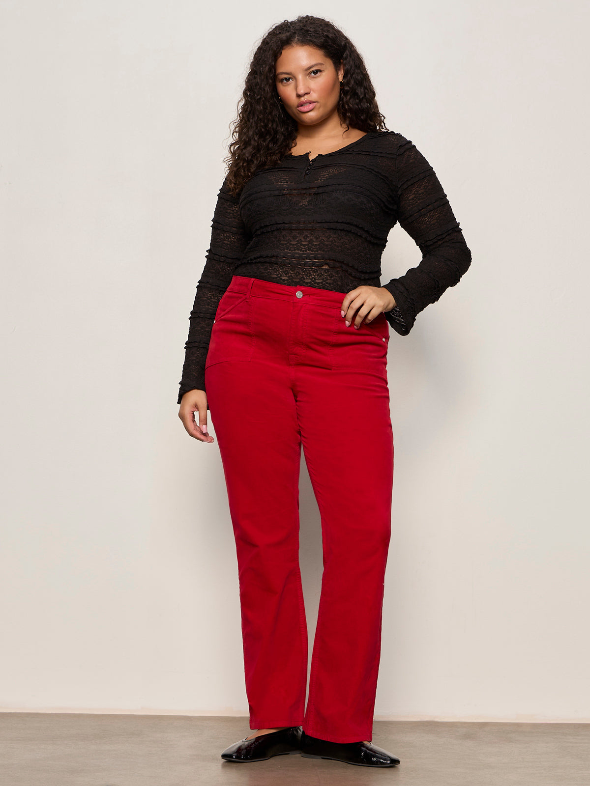 Woman wearing a black top and red pants against a plain background