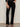 A person models the velveteen brook bootcut pant in black petites by Sanctuary Clothing, standing against a neutral background with one hand in a pocket; their head and upper body are out of frame.