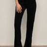 A person models the velveteen brook bootcut pant in black petites by Sanctuary Clothing, standing against a neutral background with one hand in a pocket; their head and upper body are out of frame.