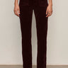 A person stands against a light background, wearing Sanctuary Clothing's velveteen brook bootcut pant in dark crimson petites, styled with black boots and a matching burgundy top; image is cropped from shoulders down.