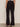 A person faces away, wearing Sanctuary Clothing's reissue peace pant in black—high-waisted cargo style with buttoned back pockets—and white heeled sandals against a plain light wall and floor.
