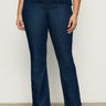 A person wears Sanctuary Clothing’s "Hayden Bootcut Jean Plot Twist" (extended sizing), featuring high-waisted dark blue denim and front patch pockets, styled with black ankle boots against a plain light background.