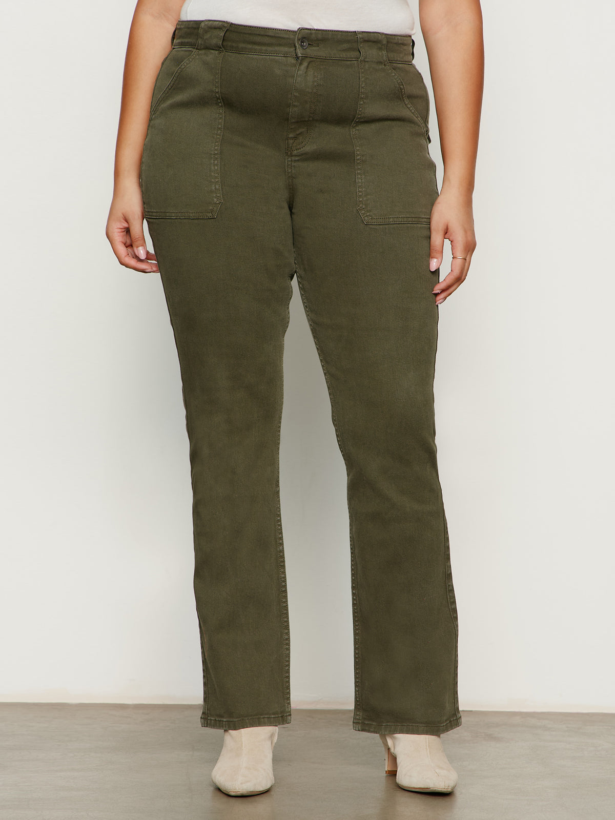 A person wearing Sanctuary Clothing's hayden bootcut jean in kalamata (extended sizing), featuring front patch pockets, paired with beige ankle boots. Only the lower torso and legs are visible against a plain background.