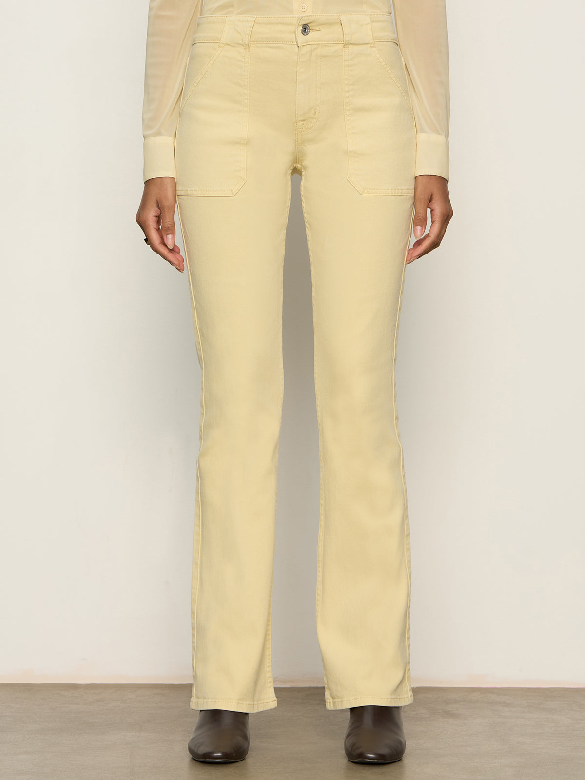 Someone wearing Sanctuary Clothing's hayden bootcut jean in buttercream, paired with a beige long-sleeve top and black ankle boots, stands against a plain light background.