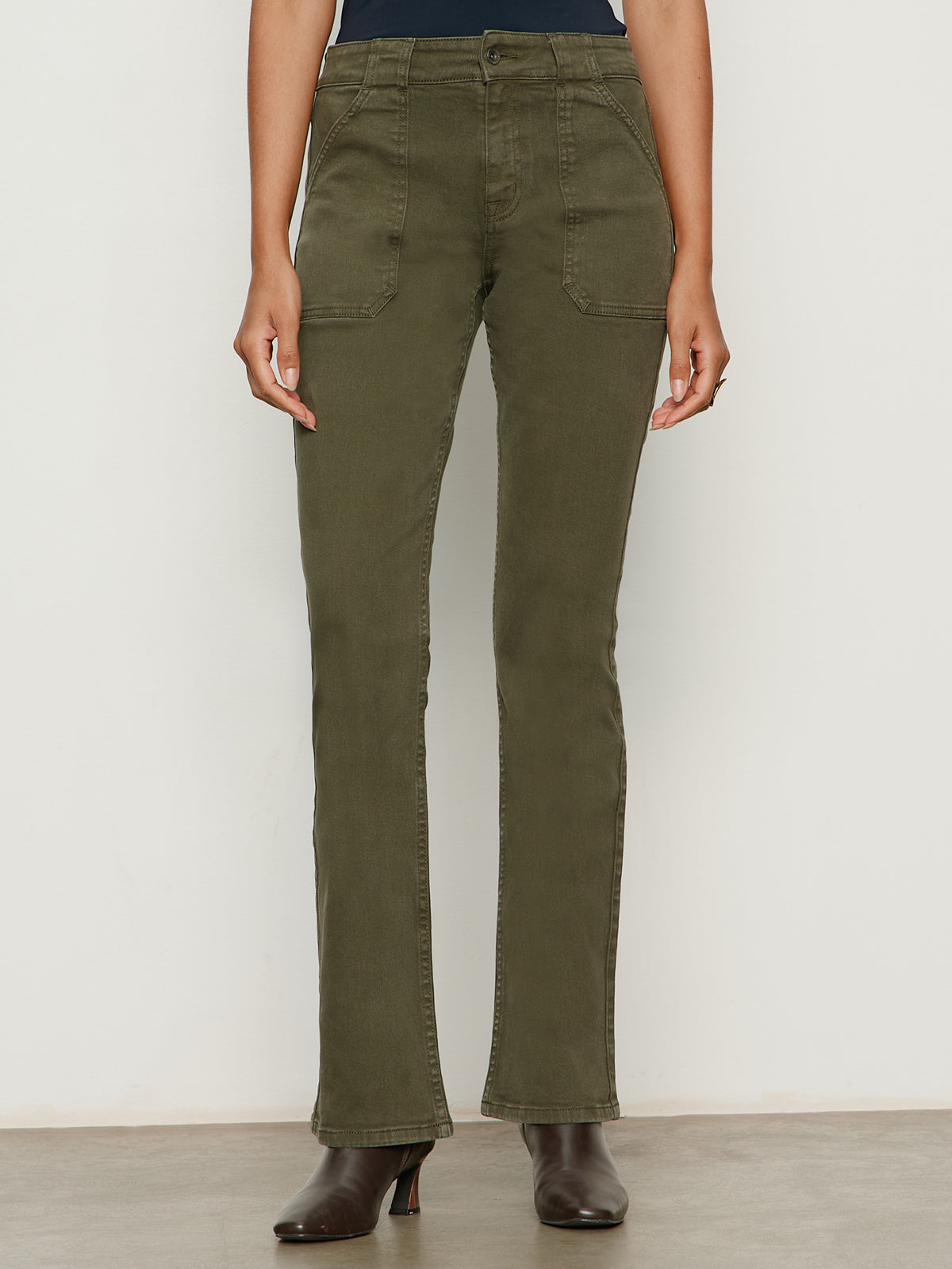 A person models the Sanctuary Clothing hayden bootcut jean in kalamata, styled with brown heeled ankle boots, standing against a plain light background.