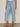 Wearing Sanctuary Clothing's retreat crop jean skyline in petite sizing, a person stands against a plain light background; the light blue, high-waisted, wide-leg jeans and tan strappy flat sandals are visible, but their upper body and face are not.
