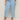 A person wearing Sanctuary Clothing's retreat crop jean skyline extended sizing in light blue, with front patch pockets, styled with a floral top and beige woven sandals, stands on a neutral floor against a plain background.