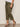 A person wears Sanctuary Clothing’s retreat crop pant in burnt olive (extended sizing), paired with a white top and black strappy heeled sandals, standing against a plain light background.