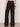 A person wearing Sanctuary Clothing shoreline linen pants in black and flat sandals stands on a gray floor, facing away from the camera, with a brown bangle on their right wrist.
