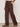 A person models Sanctuary Clothing's Shoreline Linen Pant in Rich Soil, paired with studded brown sandals and a tan clutch. The image features a plain light background and is cropped at the chest.