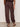 A person stands facing away, wearing Sanctuary Clothing’s melody micro linen balloon pants in rich soil with elastic cuffs and a matching top, paired with black studded sandals against a plain background.
