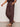 A person wears Sanctuary Clothing’s melody micro linen balloon rich soil pants—loose, dark brown with side pockets and elastic cuffs—paired with black studded flats, against a plain light background.