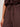 A close-up of a person wearing Sanctuary Clothing’s melody micro linen balloon pants in rich soil, featuring a high waist, loose fit, and drawstring tie, paired with a matching brown top. The person’s hand rests by their side.
