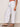 A person wearing Sanctuary Clothing's melody micro linen balloon white pants, featuring an elastic cuff and drawstring waist, stands sideways in studded black sandals against a neutral background.