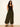 A woman with long, wavy hair wears the Sanctuary Clothing "the moment volume pant" in midnight moss, a black sleeveless top, and black sandals. She stands against a plain light-colored wall with a relaxed expression.