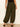 A person wearing Sanctuary Clothing’s the moment volume pant in midnight moss, featuring a loose fit and elastic cuffs, paired with black heeled sandals, stands against a light background, photographed from the back.
