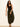 A woman with long wavy hair wears a black tank top, black sandals, and Sanctuary Clothing's the moment volume pant in midnight moss. She stands against a plain light wall, one arm relaxed and the other slightly bent.