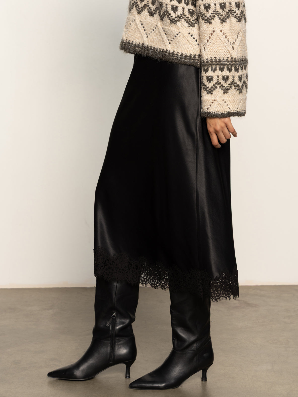 Person wearing a patterned top, black skirt, and black boots on a plain background