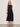 A woman stands against a light background, wearing Sanctuary Clothing’s matter of time poplin skirt in black with a sleeveless black top, necklace, brown bangle, and black sandals.