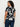 A woman with curly hair faces away, wearing Sanctuary Clothing's the perfect tee petal whisper extended sizing€”a black T-shirt with a bold white floral print€”paired with dark blue jeans against a plain white background.