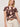 A woman with blonde, wavy, shoulder-length hair models the Sanctuary Clothing "the perfect tee desertscape" t-shirt with beige high-waisted shorts and a brown belt, standing against a plain light background and looking slightly to the side.