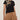 A woman wears the Sanctuary Clothing perfect tee lotus placement, a black top featuring a beige abstract floral design on the shoulder. She pairs it with loose high-waisted tan shorts and a chunky bracelet against a plain light background.