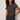 A woman with curly hair wears the Sanctuary Clothing "the perfect tee rhythmic" patterned top, paired with dark denim shorts, a brown braided belt, and brown bangles. She stands confidently against a neutral background.