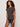 A woman with curly hair models the Sanctuary Clothing "the perfect tee rhythmic," a short-sleeve patterned blouse, paired with dark shorts and a brown bangle, against a light background.