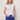 Woman wearing a white sleeveless top and blue pants against a plain background