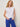 Woman wearing a white sleeveless top and blue pants against a plain background