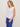 Woman wearing a white top and blue pants against a plain background