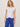 Woman wearing a white t-shirt and blue pants against a plain background