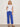 Woman wearing a white t-shirt and blue pants against a plain background