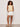 A woman with curly hair wears the Sanctuary Clothing So Twisted Muscle Tee in Banana, paired with white belted shorts and beige sandals, standing against a light-colored wall with her hands in her pockets.