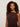 A woman with curly hair wears the Sanctuary Clothing So Twisted Muscle Tee in Rich Soil, a sleeveless top featuring a shoulder knot. She stands against a light background, looking calmly at the camera.