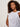 A woman with curly hair wears the Sanctuary Clothing "so twisted muscle tee" in white, featuring a knotted one-shoulder detail, standing against a plain light background and gazing calmly to the side.