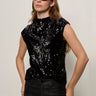 A woman wears the Sanctuary Clothing funnel neck sequin top in black, paired with black sunglasses and leather pants, standing against a plain light background with her hands in her pockets.