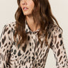 A woman with long, wavy brown hair wears the Sanctuary Clothing fitted mesh button down top mother leo, featuring a bold black and brown animal print, as she looks to her left against a plain light background.
