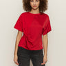 A woman with curly hair wears the Sanctuary Clothing satin mix tee in cherry lacquer, featuring short sleeves and a gathered knot detail, paired with dark jeans against a plain light background.