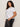 A woman with curly brown hair models the Sanctuary Clothing embellished tee in white (extended sizing) paired with dark jeans. She stands sideways, looking at the camera with a neutral expression against a plain background.
