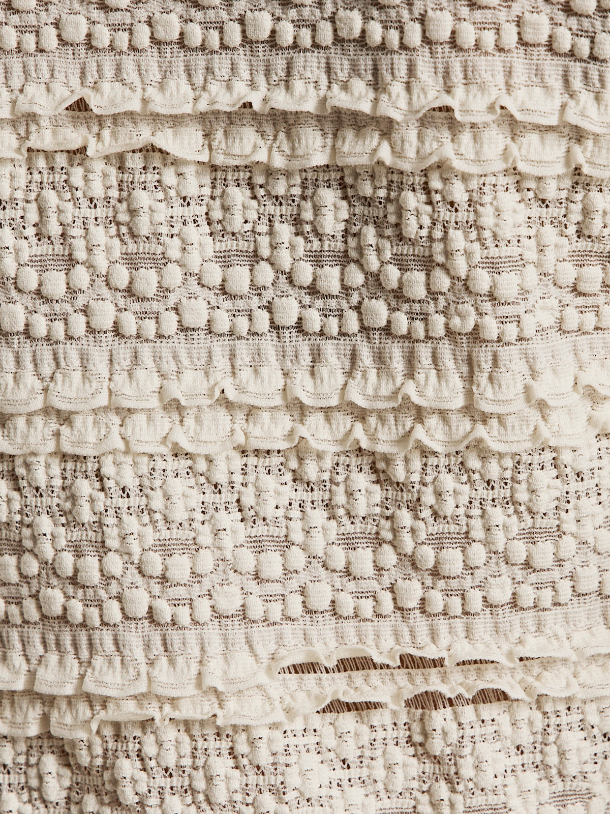 Close-up of the Sanctuary Clothing lovely lace button front top in vintage ivory, showing textured cream fabric with horizontal raised bobbles and lace-like frills for a detailed, patterned look.