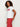 A woman with curly hair models the Sanctuary Clothing embellished tee in white w cherry lacquer, paired with high-waisted red pants, standing sideways and looking at the camera against a plain white background.