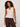 A woman with curly hair wears the Sanctuary Clothing friday rib tank collagen, a sleeveless beige henley top, and loose dark brown pants, accessorized with bangles and a necklace against a plain light background.