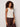 A woman with curly hair models the Sanctuary Clothing friday rib tank collagen, a sleeveless cream top, paired with dark brown pants. She stands against a plain light background, looking at the camera with a slight smile.