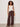 A woman with curly hair poses confidently against a plain background, wearing Sanctuary Clothing's Friday Rib Tank Collagen, loose brown drawstring pants, black sandals, and yellow bangles.