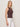 A woman with blonde hair models the Sanctuary Clothing friday rib tank in rich soil—a sleeveless brown button-up top—paired with high-waisted white pants against a plain light background, facing slightly to the side and looking at the camera.