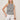 A woman with blonde hair wears the Sanctuary Clothing campari tank macrame stripe top and white lace-up pants, standing against a plain light background with a brown bangle on her wrist.